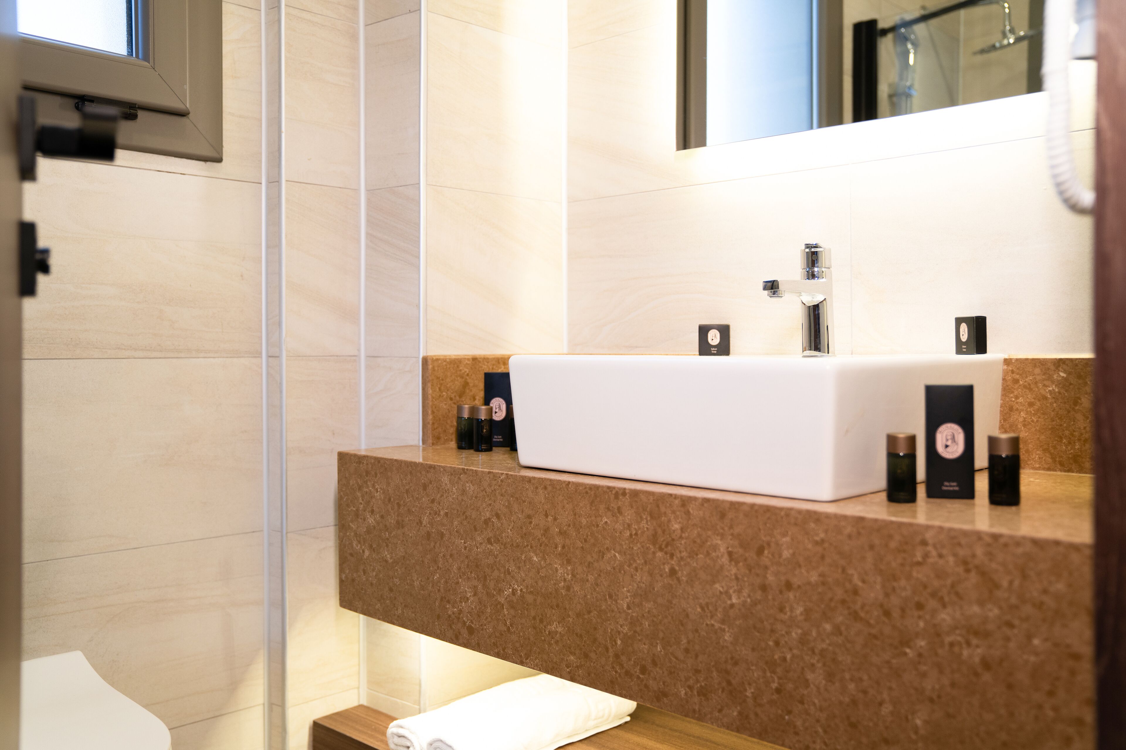 A modern bathroom with a white sink, a mirror, and a towel on a wooden shelf.