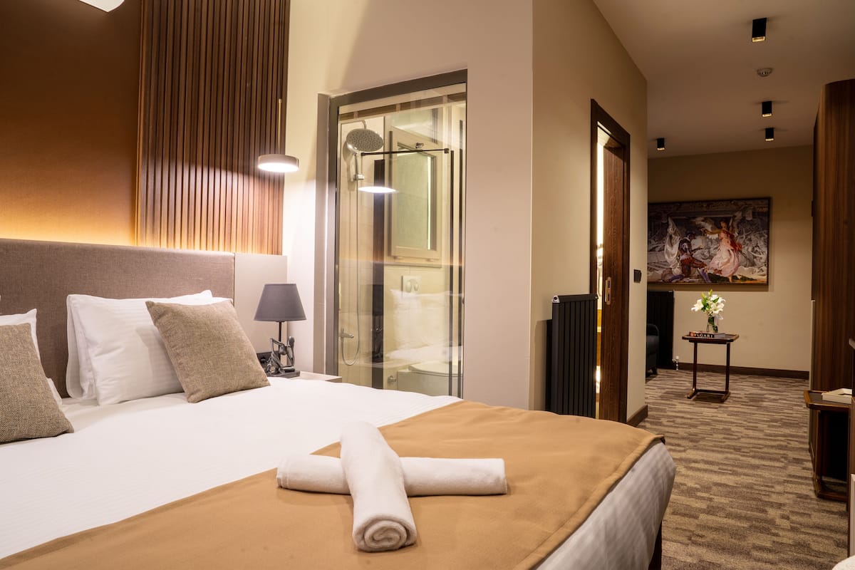 Ein Hotelzimmer mit einem großen Bett, einer Duschkabine aus Glas, einem Gemälde an der Wand und einem kleinen Tisch mit einem Schild.