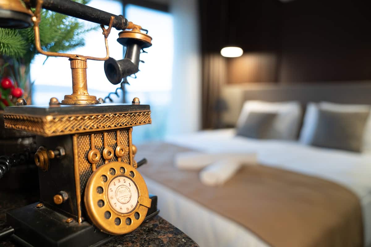 Ein altes Telefon auf einem Tisch in einem Hotelzimmer, mit einem Bett und einem Nachttisch.