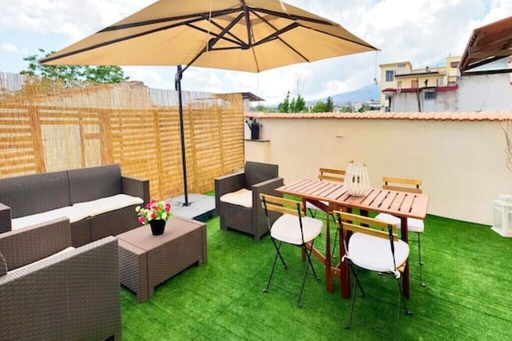 Eine Terrasse im Freien mit Tisch und Stühlen, einer Sitzecke und einem großen Sonnenschirm.