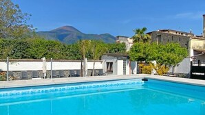 A swimming pool with a mountain backdrop, surrounded by greenery and buildings. - Terrace over VESUVIO/Pompei - Elizabeth's Suite (Terzigno)