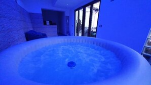 A hot tub in a room with a stone wall and a glass door leading outside. - Terrace over VESUVIO/Pompei - Elizabeth's Suite (Terzigno)