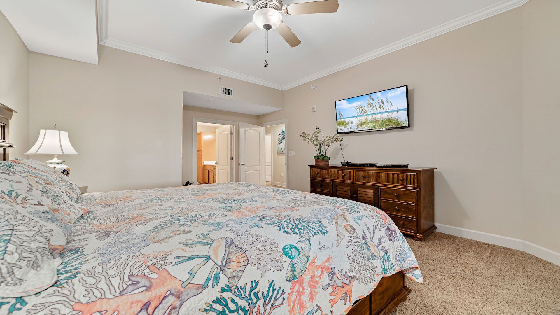 A bedroom with a bed, a ceiling fan, a dresser, and a television on the wall.
