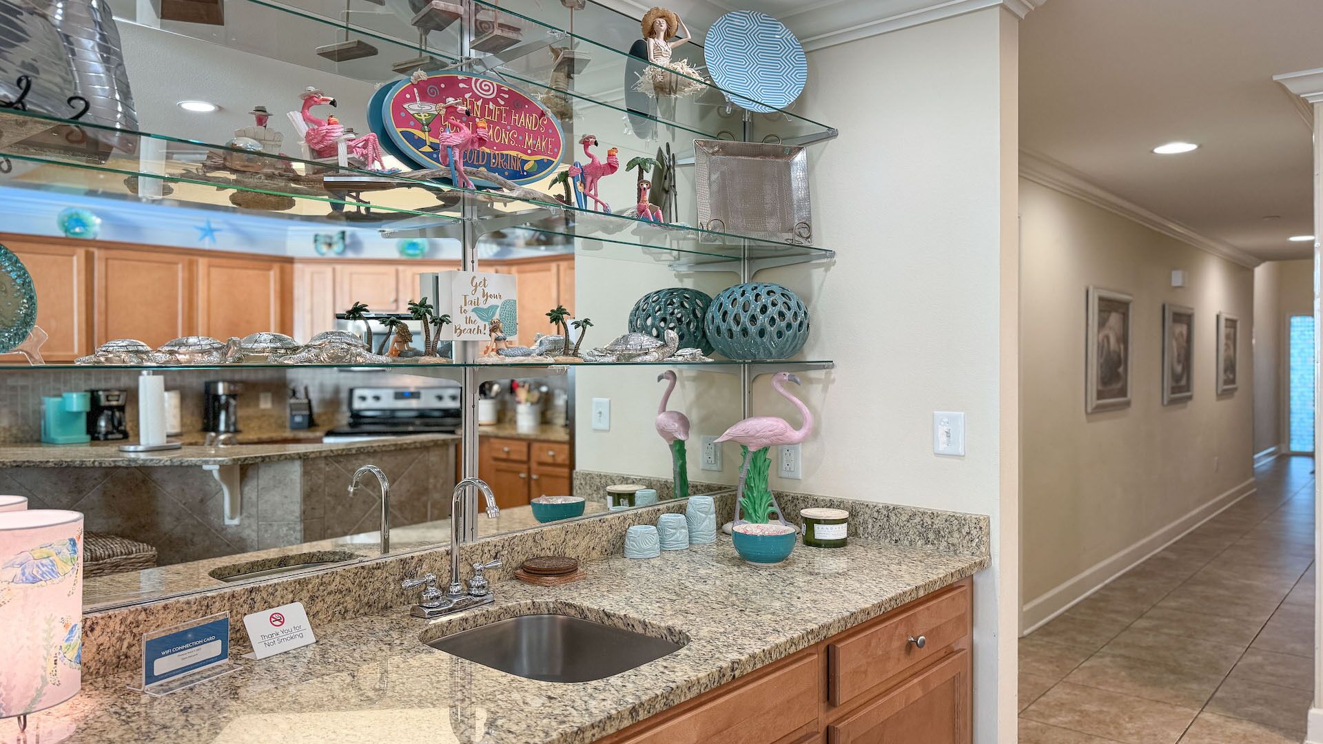 Una cocina con encimeras de granito, un lavamanos de acero inoxidable y elementos decorativos como flamencos y un letrero que dice '¡Ve a la playa!'