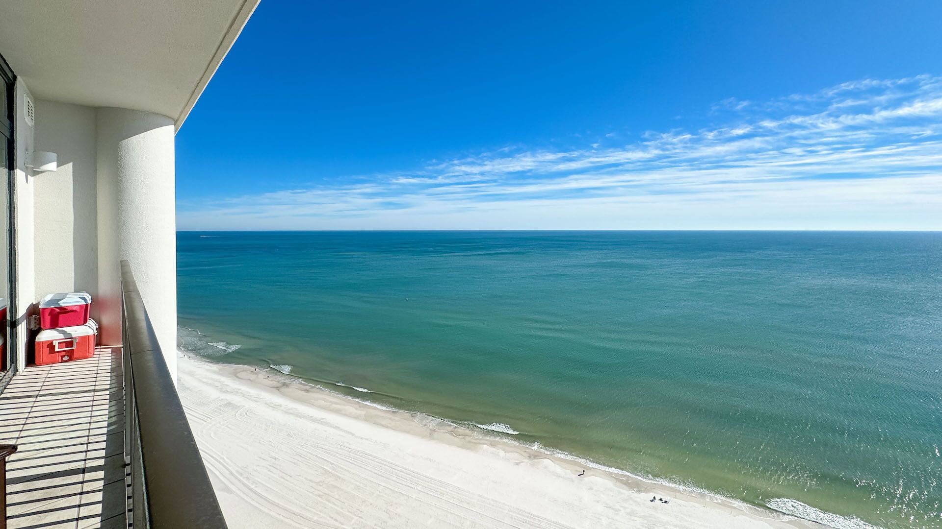 A balcony with a view of the ocean, a sandy beach, and a clear sky.