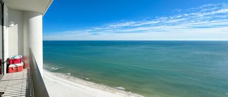 A balcony with a view of the ocean, a sandy beach, and a clear sky.