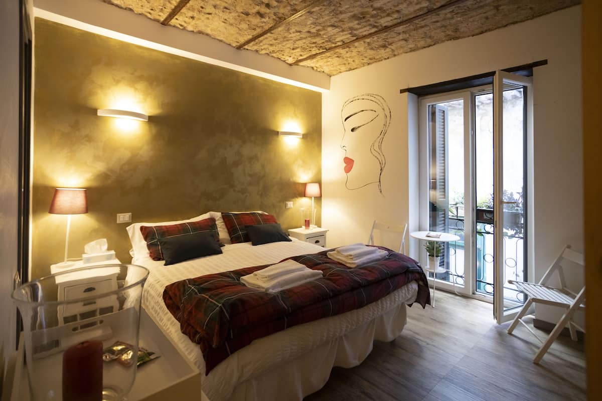 Une chambre à coucher avec un grand lit, deux tables de chevet, une commode, un vase en verre et un balcon avec une chaise.