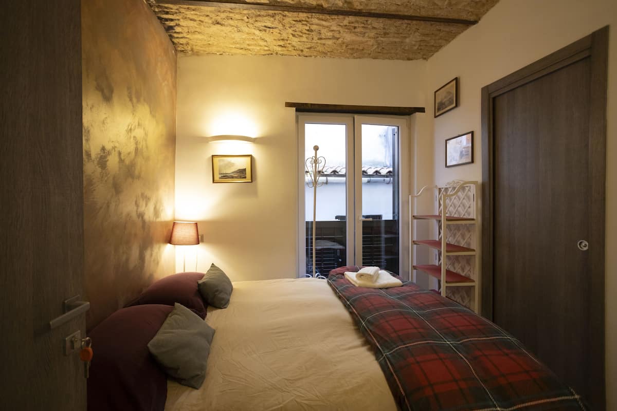Une chambre à coucher avec un lit, une table de chevet, une lampe, une fenêtre donnant sur un paysage agréable et une porte.