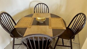 Una mesa redonda de comedor con un mantel a cuadros y un centro de mesa con un cuenco dorado. Cuatro sillas negras rodean la mesa.