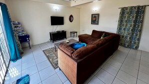 Una sala de estar con un sofá marrón, un televisor, un ventilador de techo y una cortina estampada.