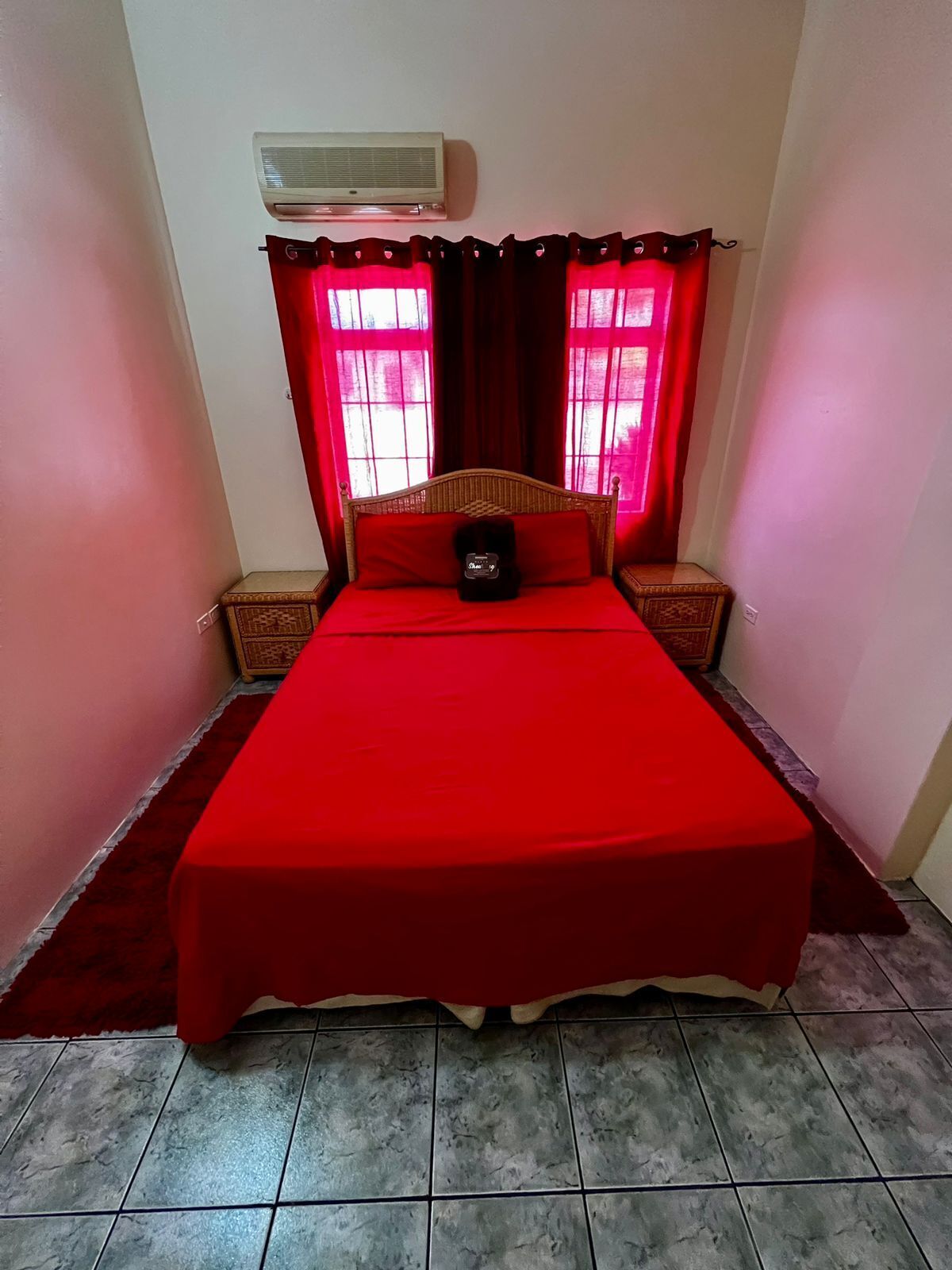 A bedroom with a large bed, red curtains, a wall-mounted air conditioner, and two nightstands.