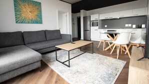 A modern living room with a grey sectional sofa, a wooden coffee table, and a large abstract painting on the wall. - 9 Palms by Smart City Stays (Cape Town)