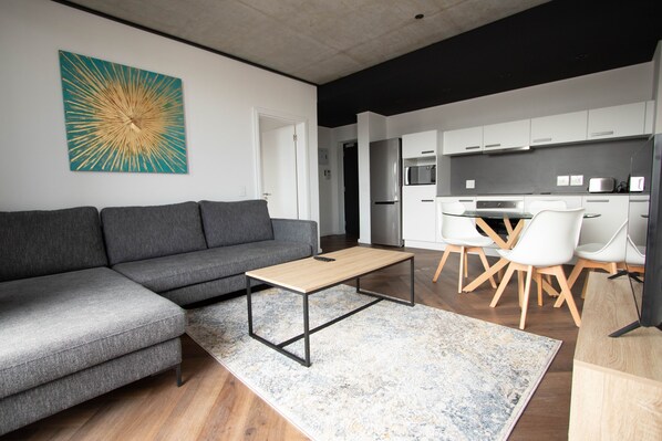 Un salon moderne avec un canapé d’angle gris, une table basse en bois et un grand tableau abstrait accroché au mur.