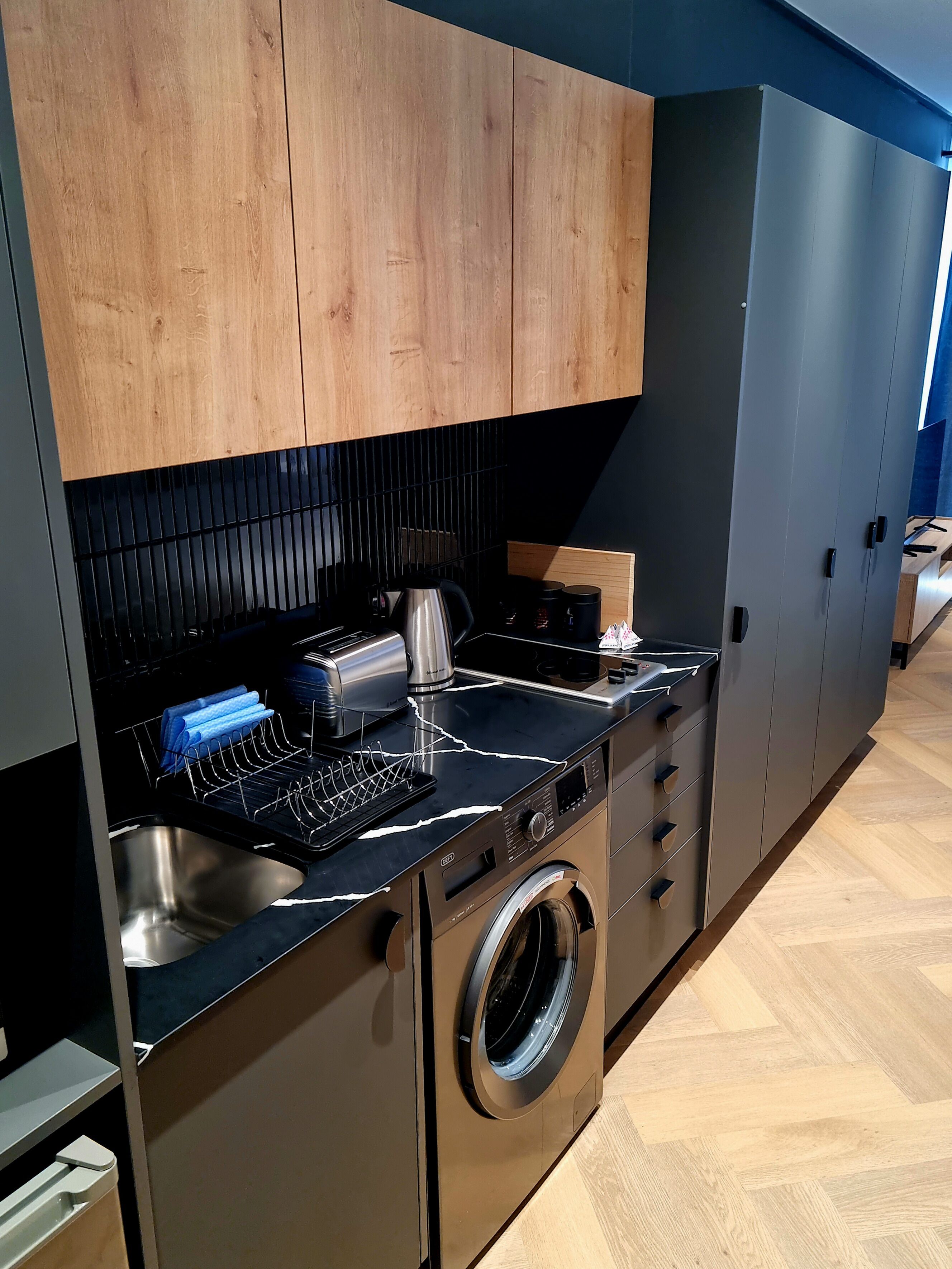 Uma cozinha compacta com armários de madeira, forno embutido, máquina de lavar e pia de aço inoxidável.