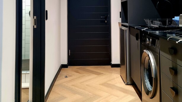 A modern kitchen with a washing machine, a black door, and wooden flooring. - 9 Palms by Smart City Stays (Cape Town)