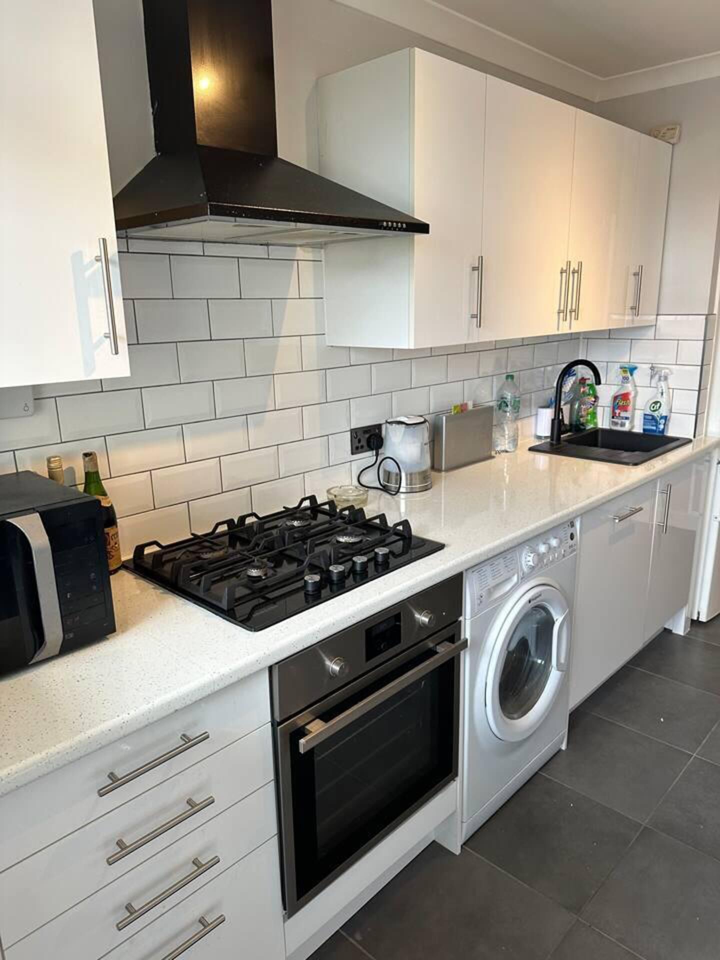 Une cuisine moderne avec des meubles blancs, une cuisinière à gaz, un four encastré et un lave-linge.