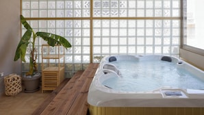 Een wellnessruimte met een jacuzzi, houten vloeren, een kamerplant en een raam met geëtste glaspanelen.