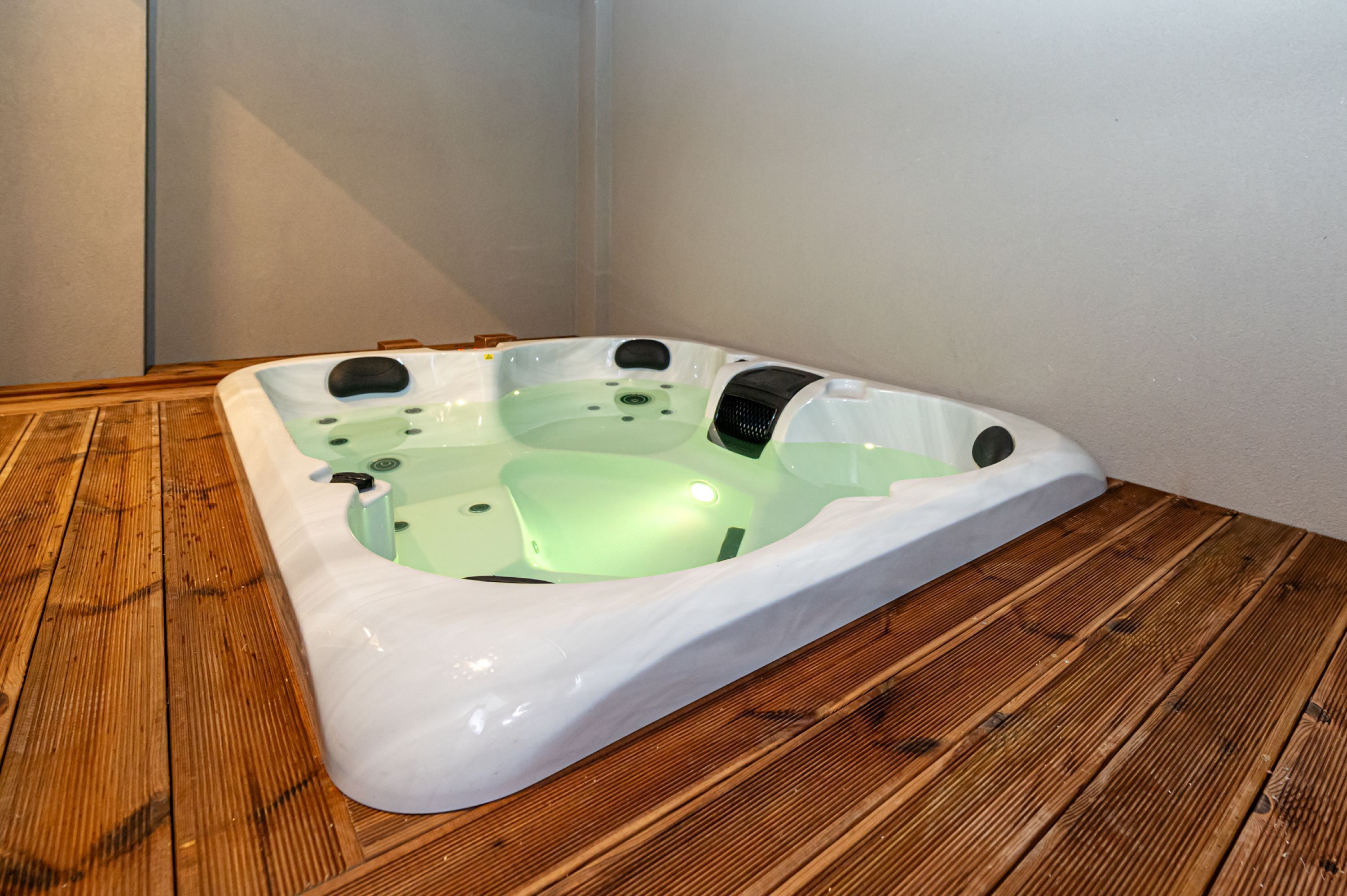 En rektangulær jacuzzi med lysegrøn indvendig, placeret på en træterrasse.