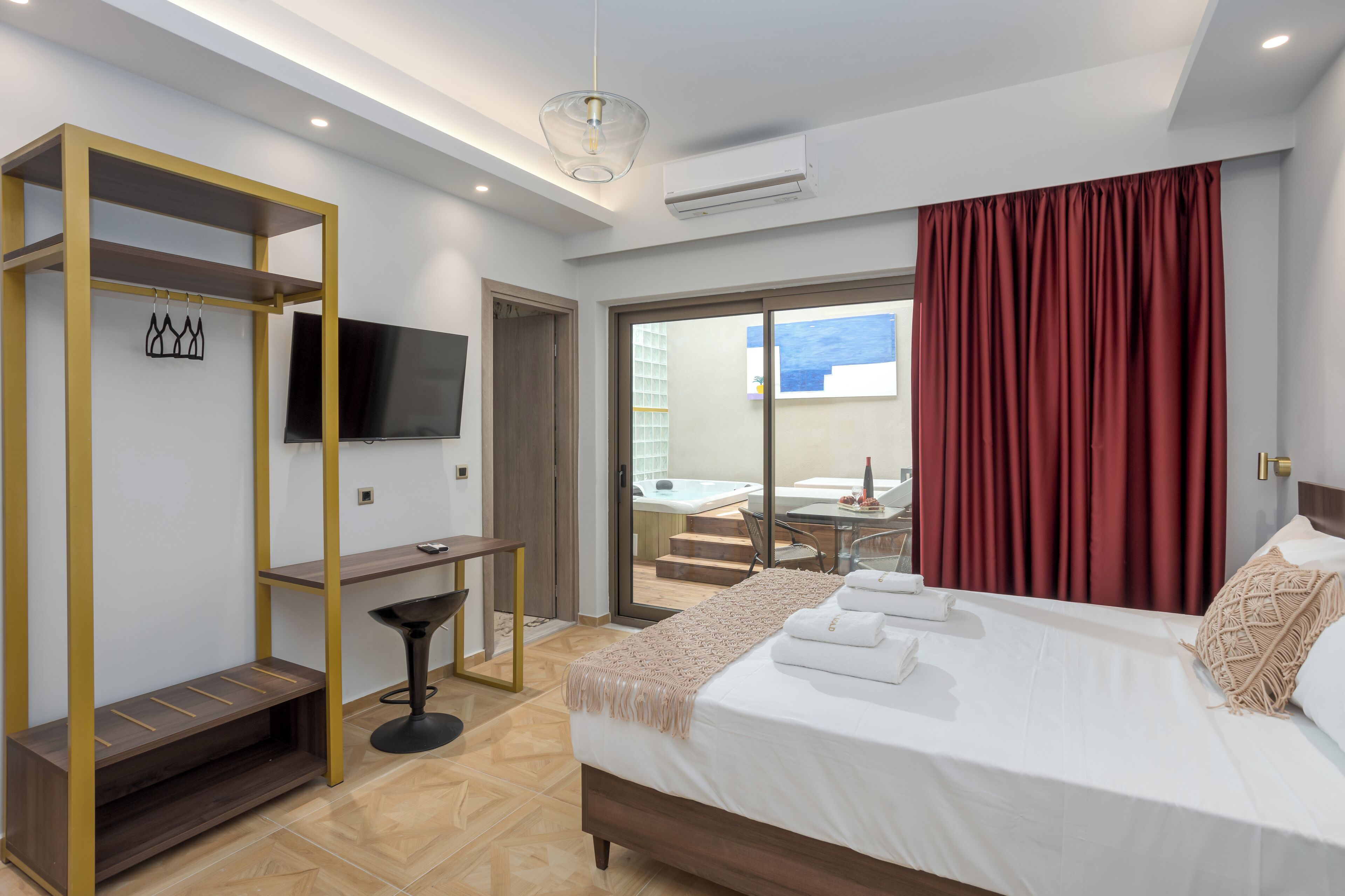 A modern hotel room with a bed, a desk, a TV, and a balcony with red curtains.