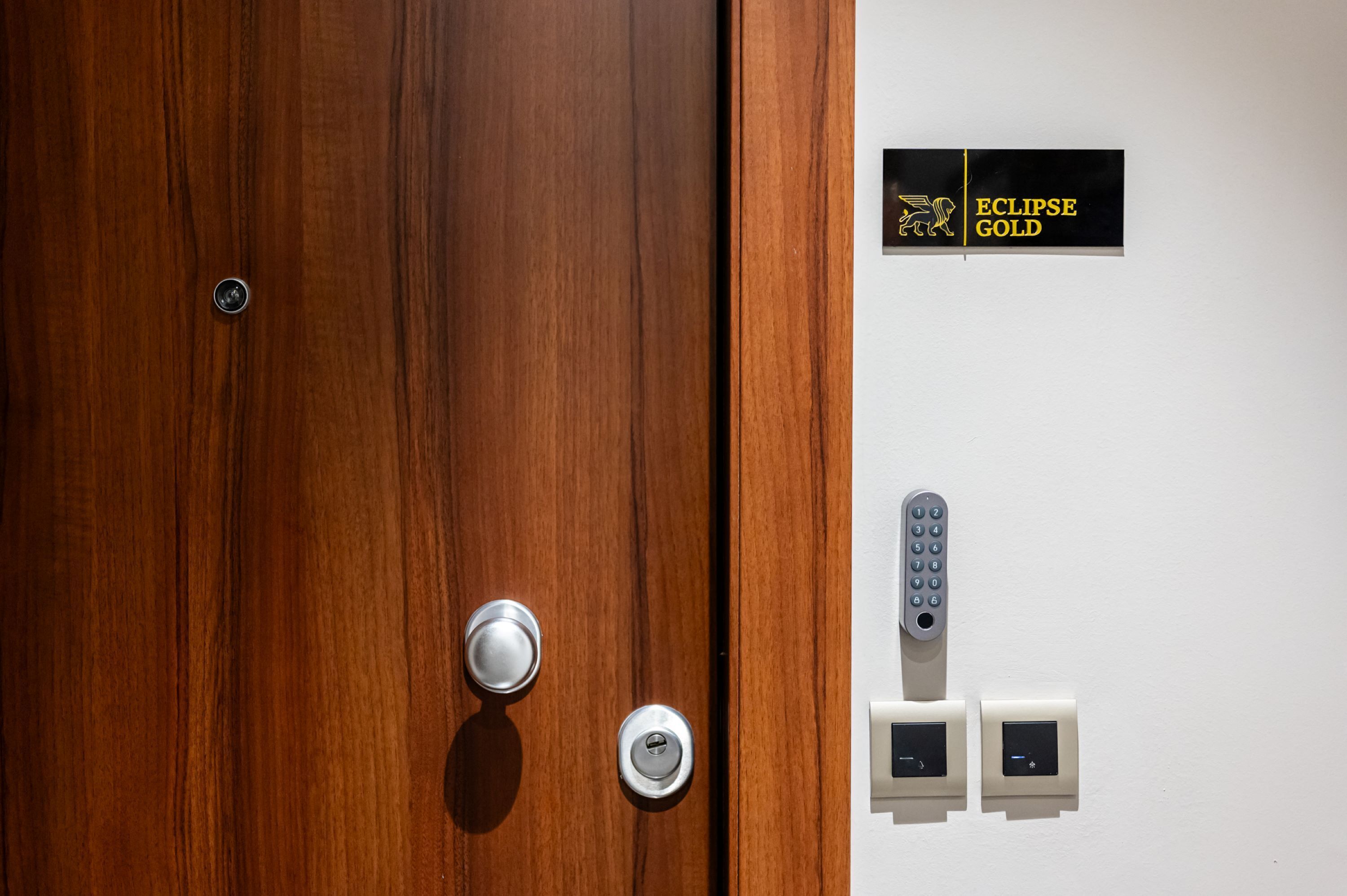 Una puerta de madera con un ojo de cerradura y cerradura, un teclado numérico y dos paneles de control en la pared.