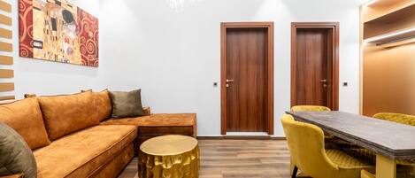 A modern living room with a sofa, a round gold table, and yellow chairs. There is a wooden door and a painting on the wall.