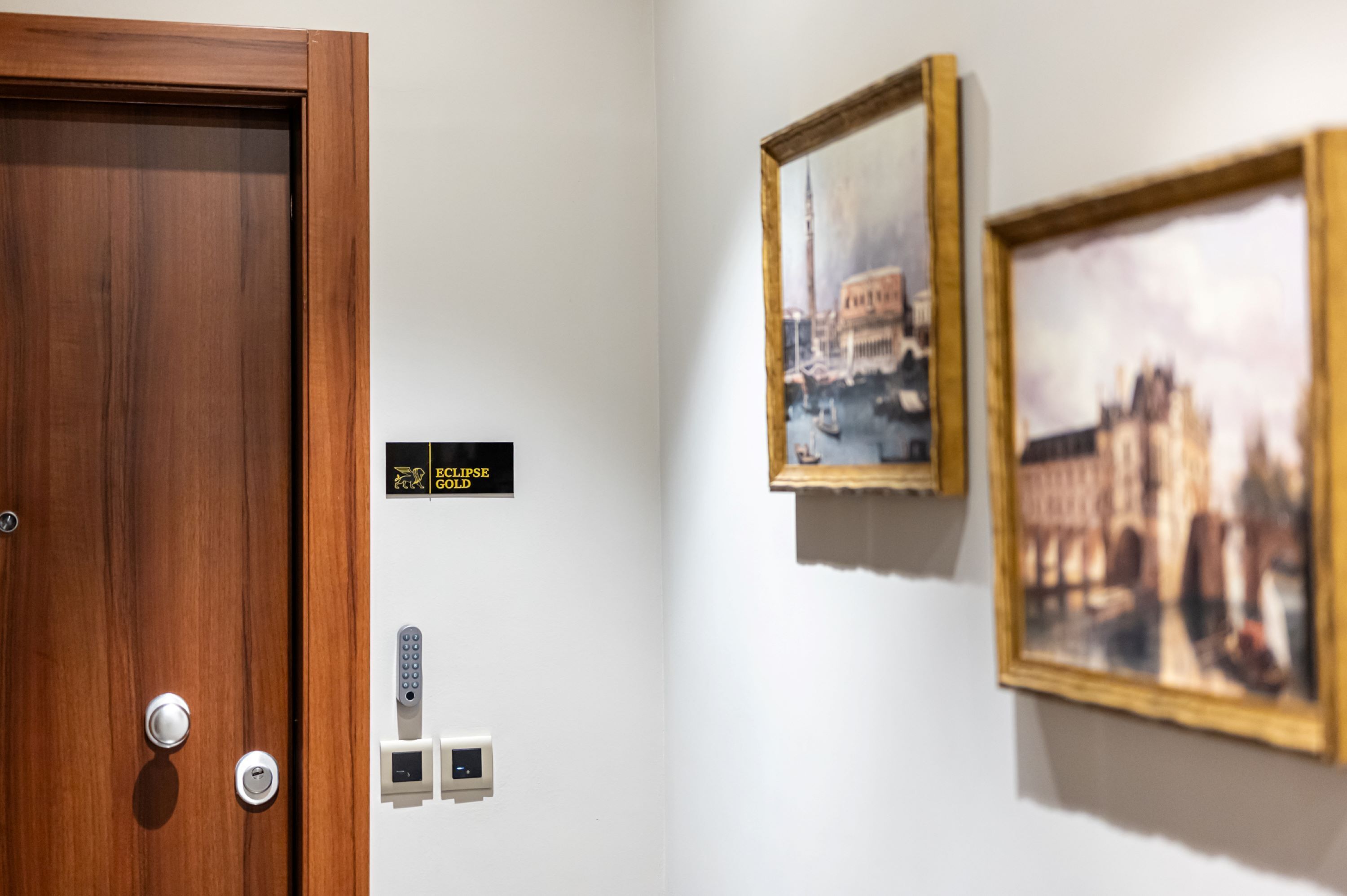 A hotel room with a wooden door, a keycard reader, a digital lock, and two framed pictures on the wall.