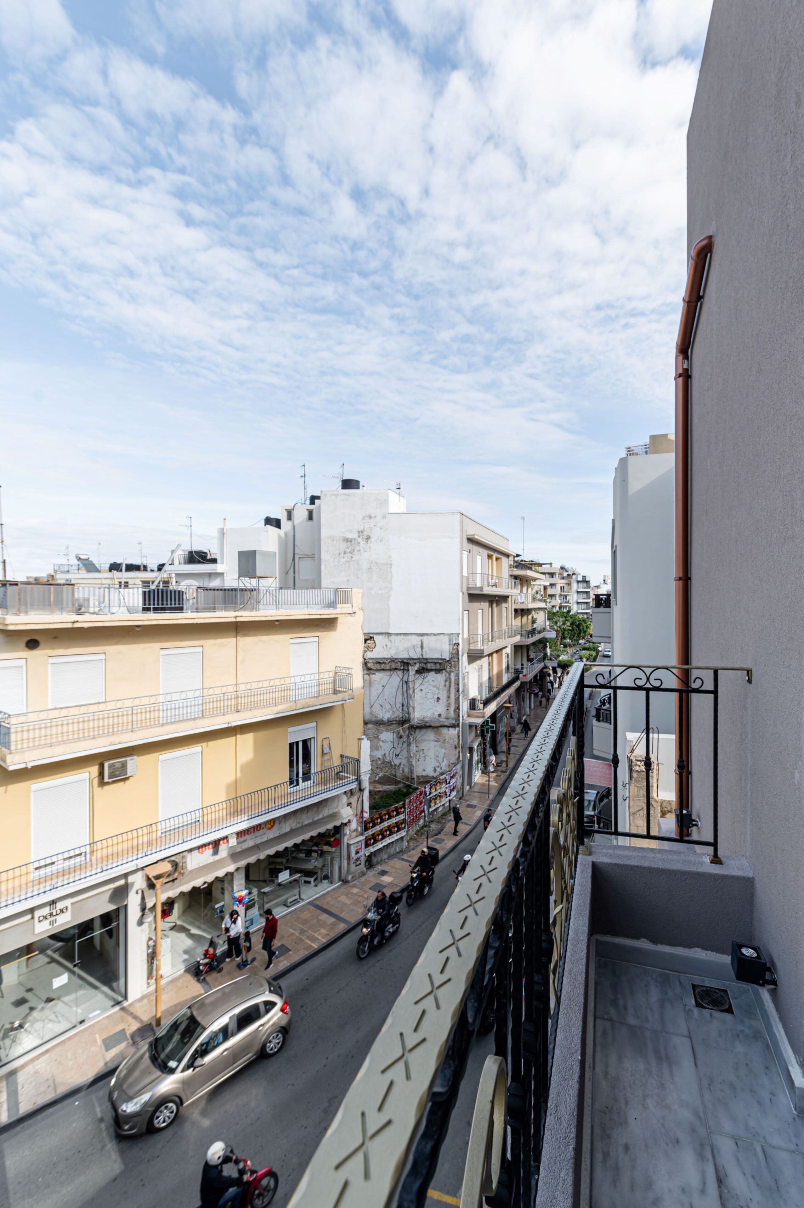 Straatbeeld vanaf een balkon, met uitzicht op een stadsgel met gebouwen, een geparkeerde auto en een motor.