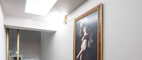 A staircase with marble steps and a yellow handrail, leading to a landing with a framed artwork on the wall.