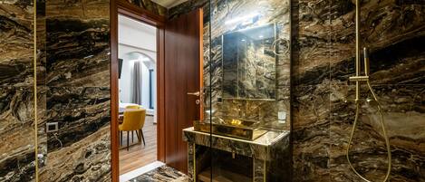 A bathroom with a marble vanity, a gold showerhead, and a mirror.
