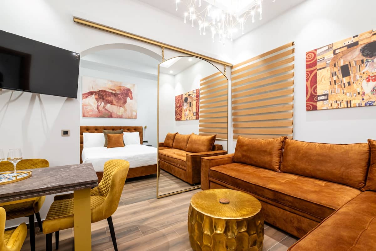 Una habitación de hotel moderna con cama, sofá, mesa de comedor, sillas y televisor.