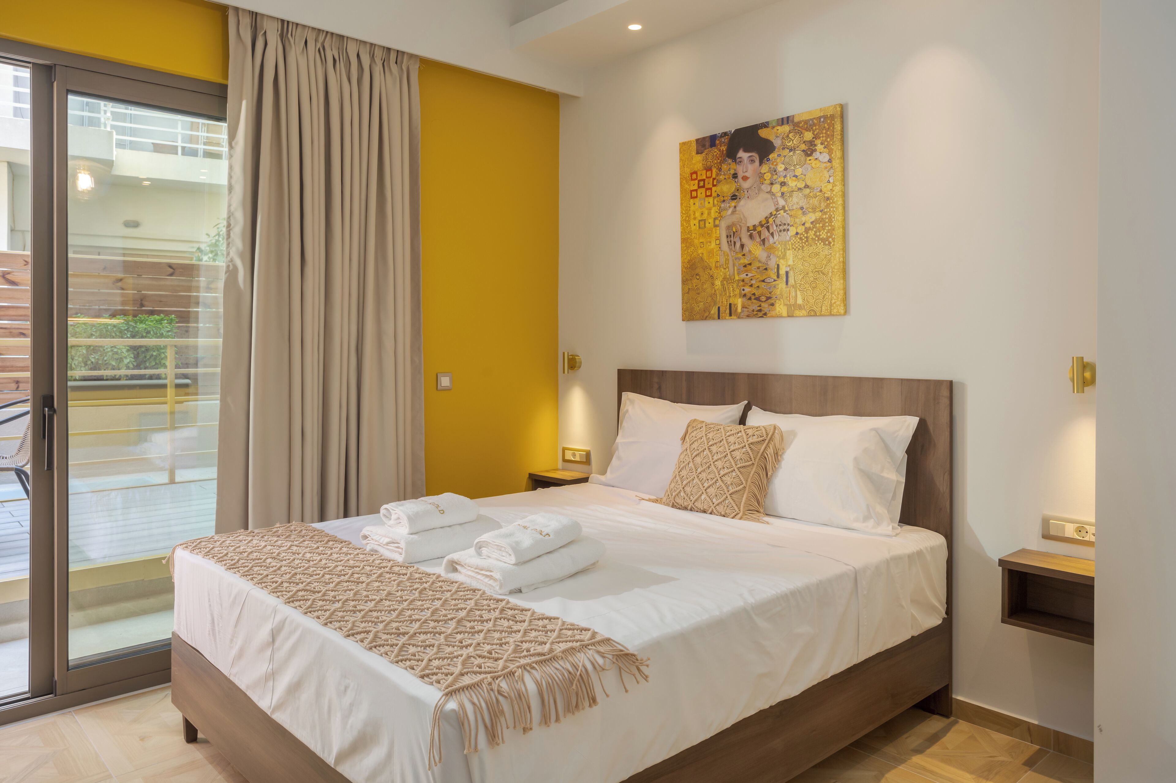 A hotel room with a large bed, a sliding glass door to a balcony, a painting on the wall, and a small bedside table.