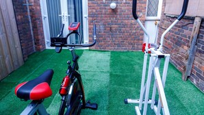 A stationary bike and an elliptical machine in a backyard with artificial grass, a brick wall, and a wooden fence. - Inviting 3-bed House in London, Stay up to 6 (London)