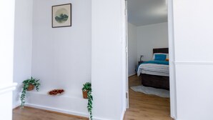 A room with a bed, a nightstand, a wall-mounted picture, and two potted plants. - Inviting 3-bed House in London, Stay up to 6 (London)