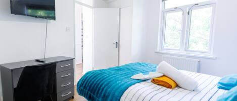 A modern bedroom with a bed, a desk, and a TV.