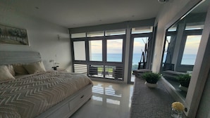 A bedroom with a bed, a nightstand, a potted plant, and a view of the sea through large windows. - Torremar Luxury Villa: A Luxurious Coastal Escape for Adults (Isabela)