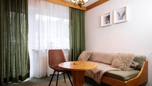A cozy living room with a wooden sofa, a round wooden table, and a chair. There are two framed pictures on the wall.