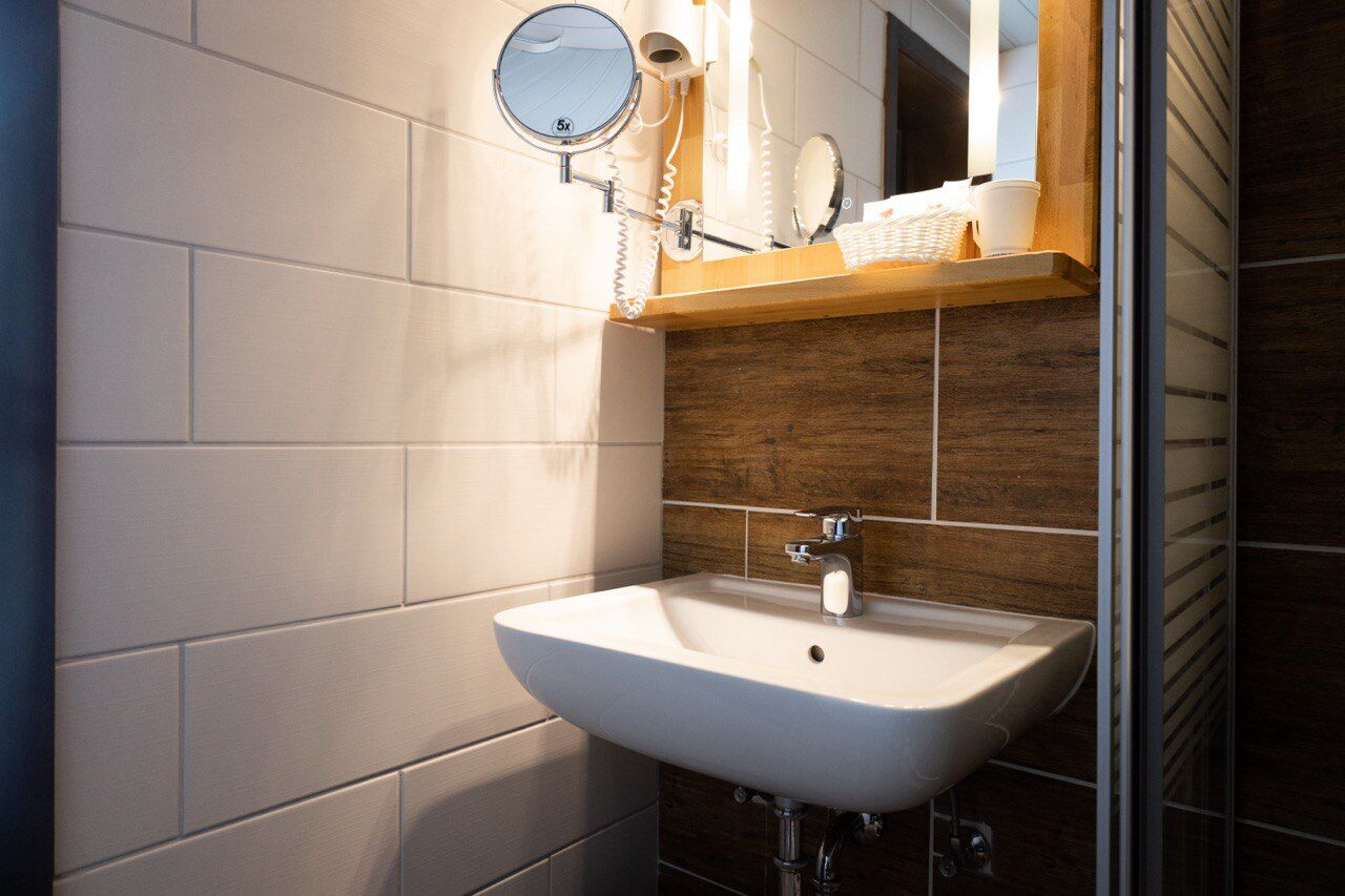 A bathroom with a white sink, wooden vanity, and a mirror with a magnifying glass.