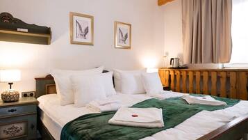 A neatly made bed with white linens and a green throw blanket, a bedside table with a lamp and a decorative item, and two framed pictures on the wall.