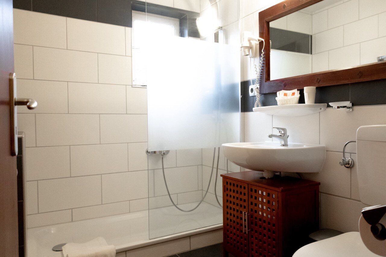Un baño con lavamanos blanco, un mueble de madera, un espejo y una zona de ducha.