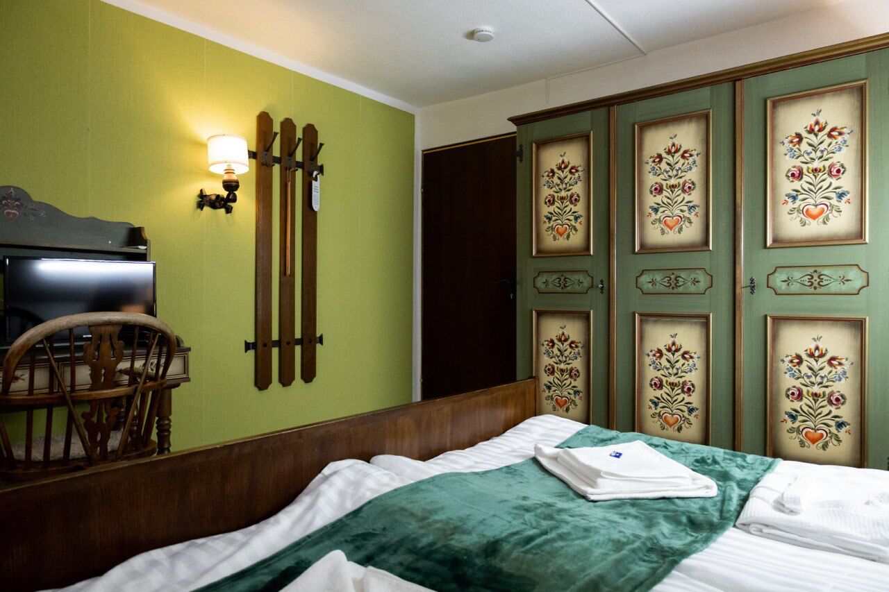 Una habitación de hotel con cama, una silla de madera, un televisor y un armario con diseños florales.