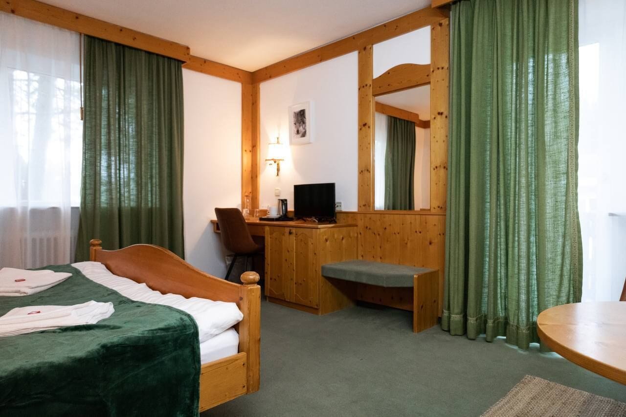 Hotellihuone, jossa on sänky, työpöytä, tuoli, tietokone ja pyöreä pöytä.