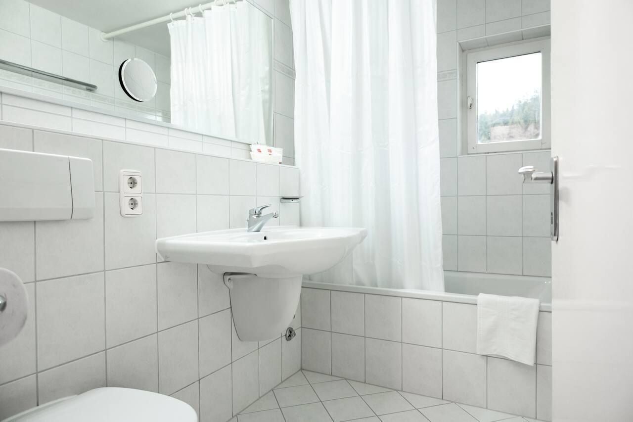Un baño moderno con lavamanos, inodoro y zona de ducha blancos.