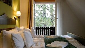 A hotel room with a bed, pillows, a green blanket, a wall-mounted lamp, and a window with a view of trees.
