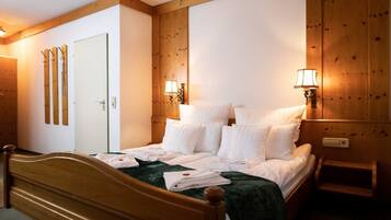 Une chambre d’hôtel avec un lit en bois, du linge de lit blanc, deux lampes fixées au mur et une armoire en bois.
