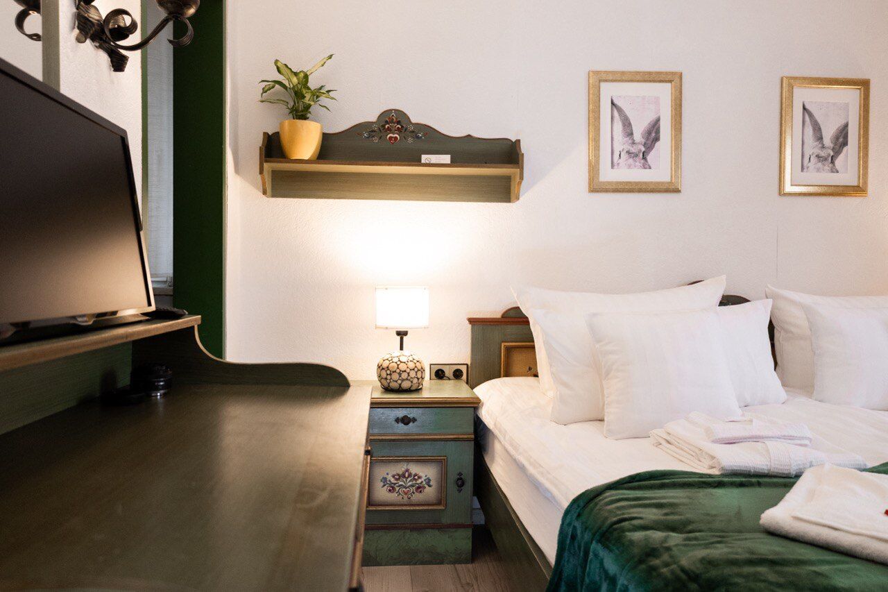 Una habitación de hotel con cama, mesita de noche, lámpara y estante en la pared con una planta.