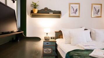 Una habitación de hotel con cama, mesita de noche, lámpara y estante en la pared con una planta.