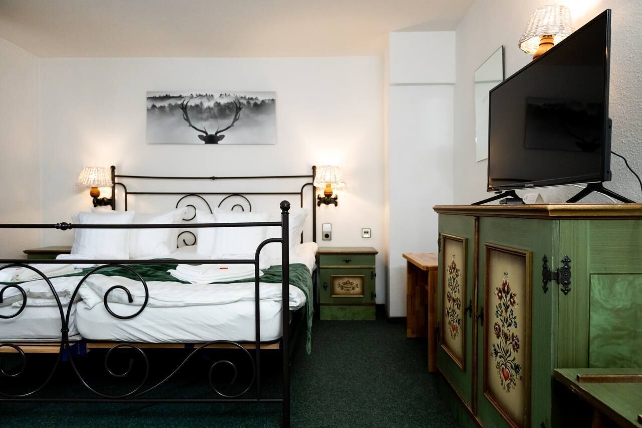 A bedroom with a bed, bedside lamps, a television, a cabinet, and a painting on the wall.