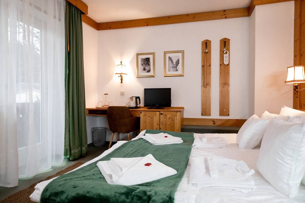 A hotel room with a bed, a desk, a television, and two framed pictures on the wall.