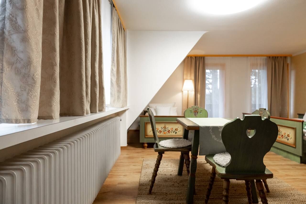 Une pièce chaleureuse avec un plafond en pente, une table en bois avec des chaises, un radiateur et une fenêtre avec des rideaux.