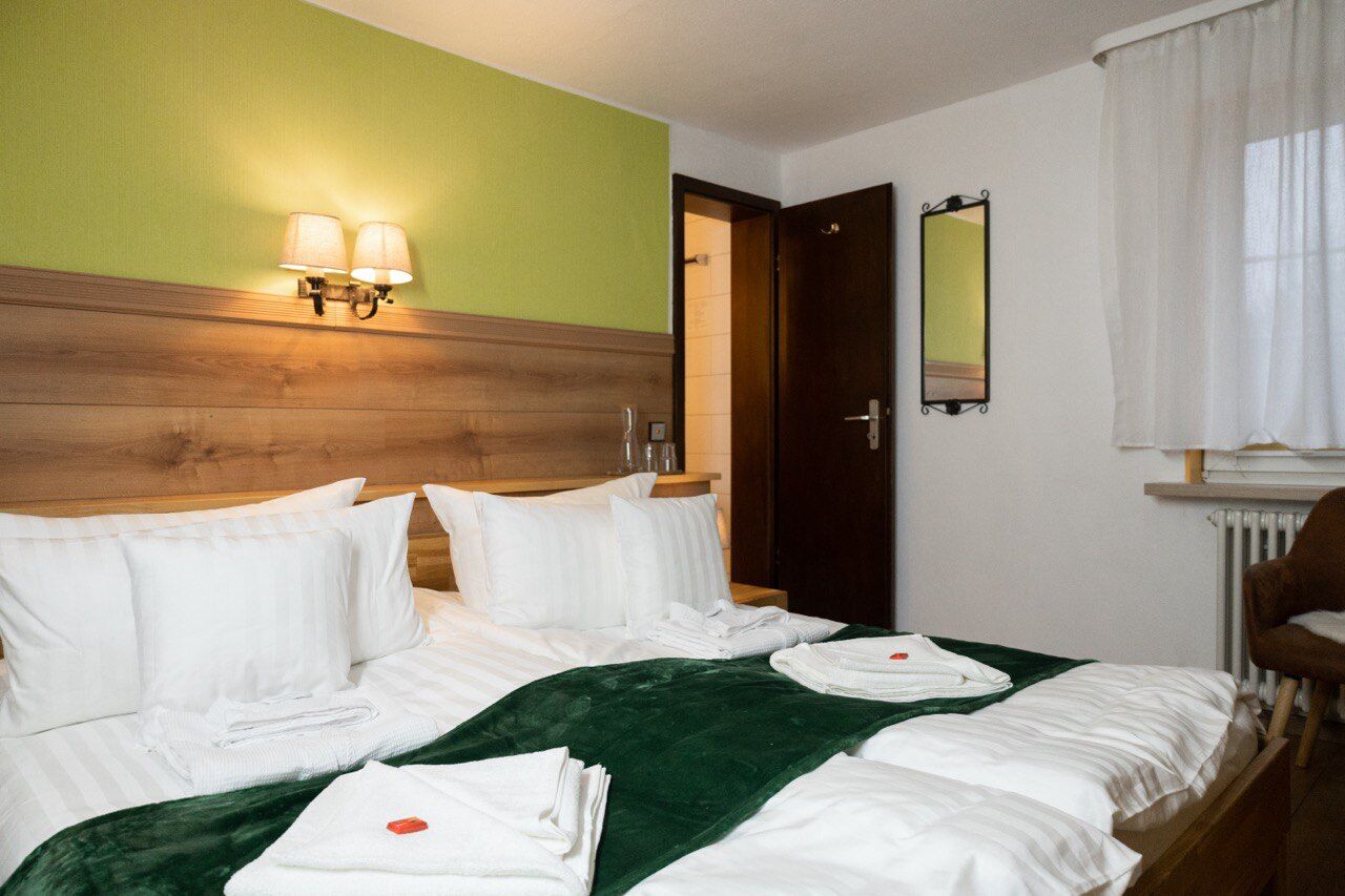 Une chambre d’hôtel avec une tête de lit en bois, deux lampes de chevet, un plaid vert et des serviettes soigneusement pliées sur le lit.